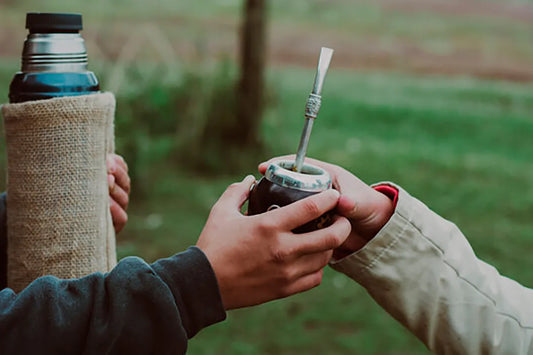 Personas pasándose un mate con un termo de agua caliente de fondo