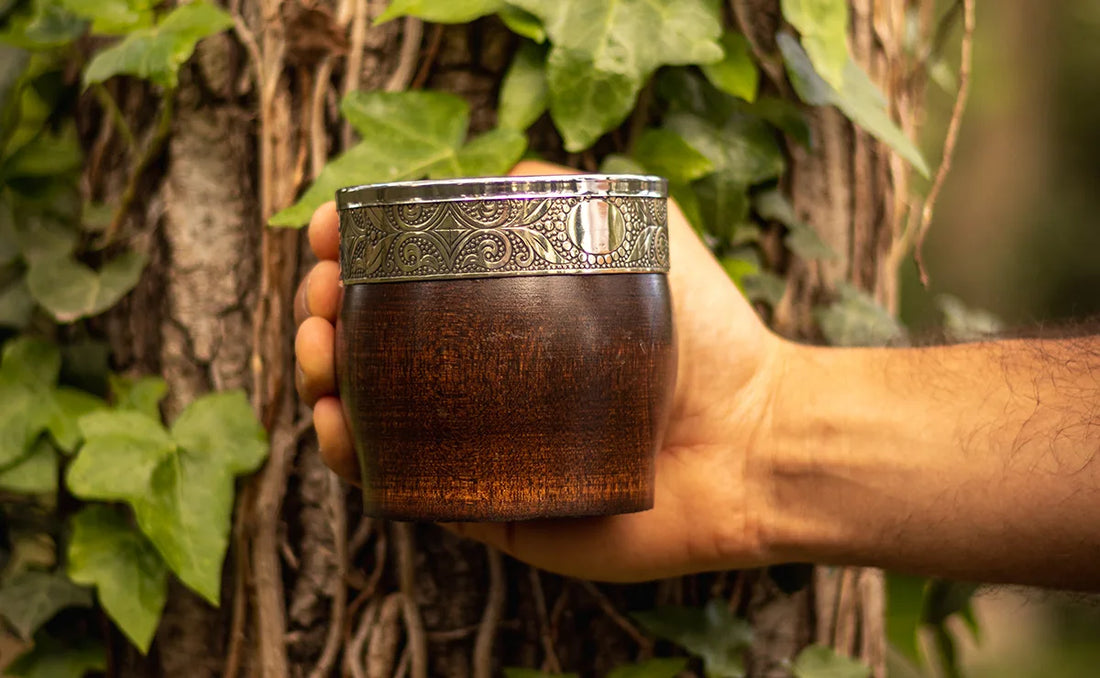 Mate de madera con virola de acero sobre fondo de hojas verdes