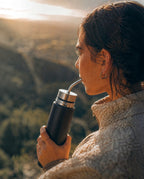 Mujer bebiendo de un Mate Listo Boldo de acero inoxidable negro en un entorno natural al atardecer