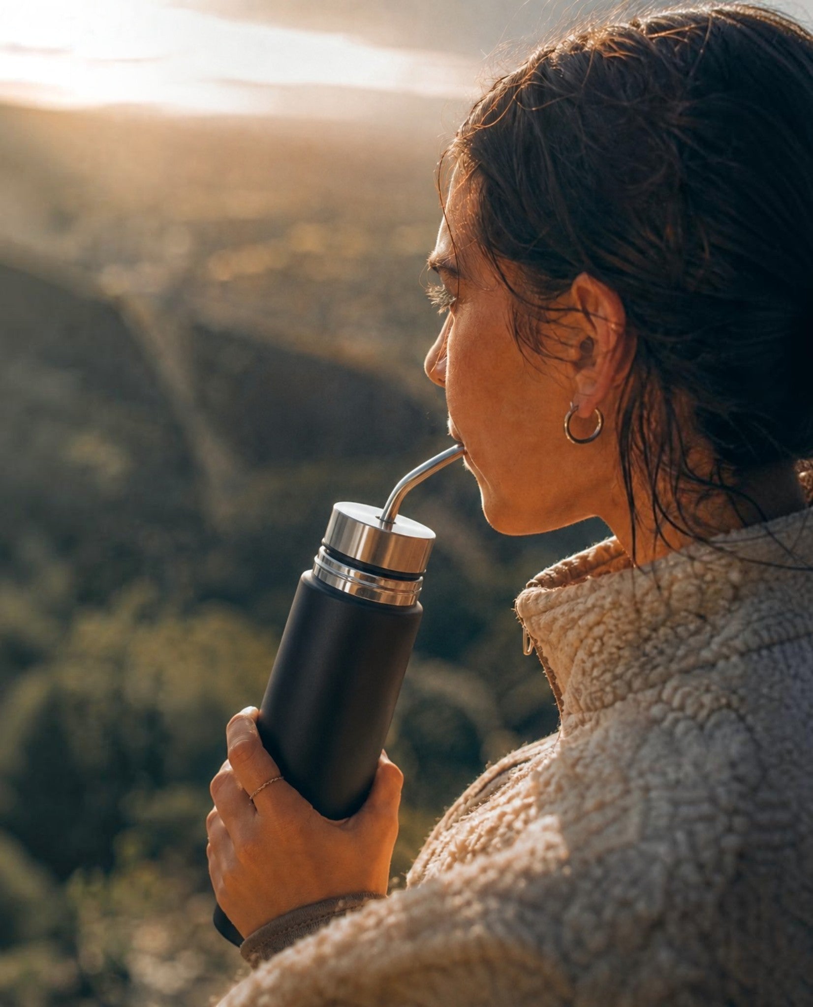 Mujer bebiendo de un Mate Listo Boldo de acero inoxidable negro en un entorno natural al atardecer
