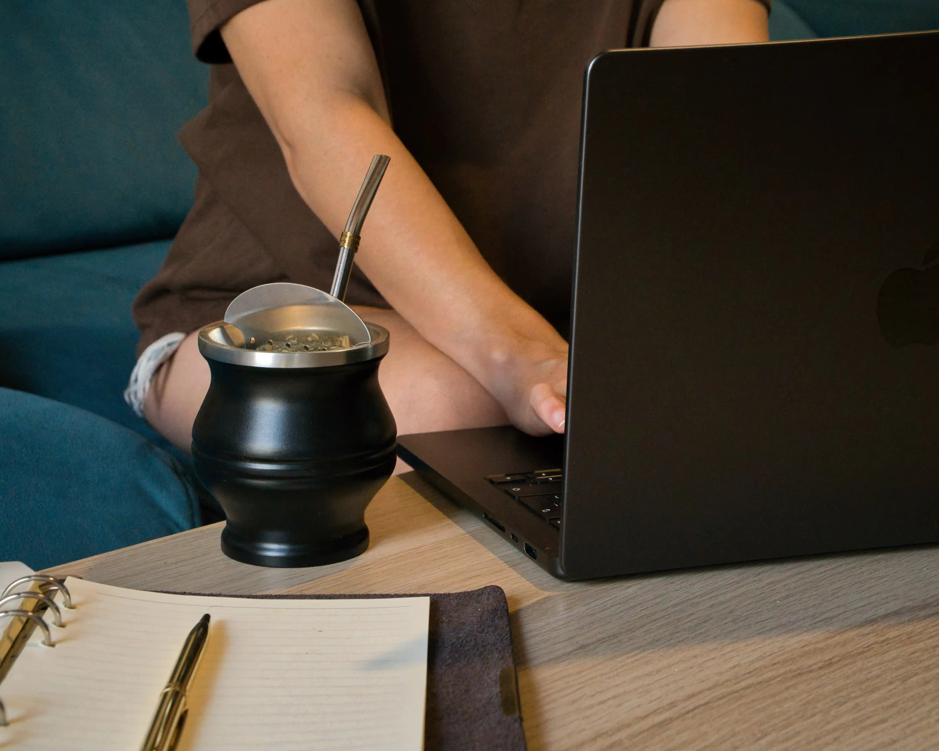 Mate sobre el escritorio junto a un cuaderno mientras se trabaja con el portátil